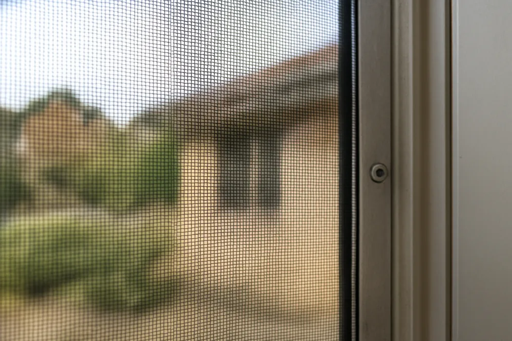 The edge of a metal mesh screen fixed to an aluminium window frame — bushfire screens and mesh, Adelaide Hills. Illustrative example.